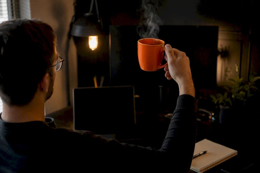 Hand holding steaming orange coffee mug